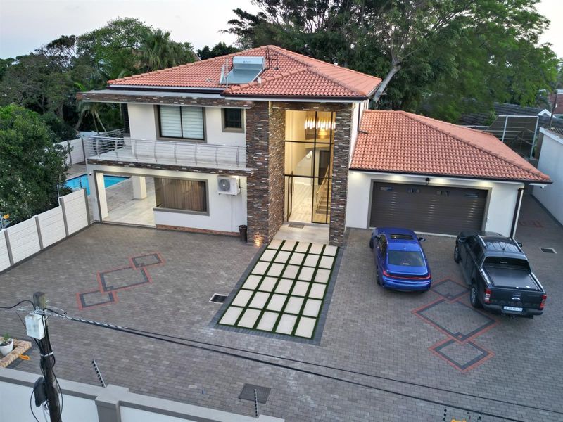 Aerial view of a modern two-story house featuring a tiled roof, stone cladding, paved driveway, double garage, and a balcony.