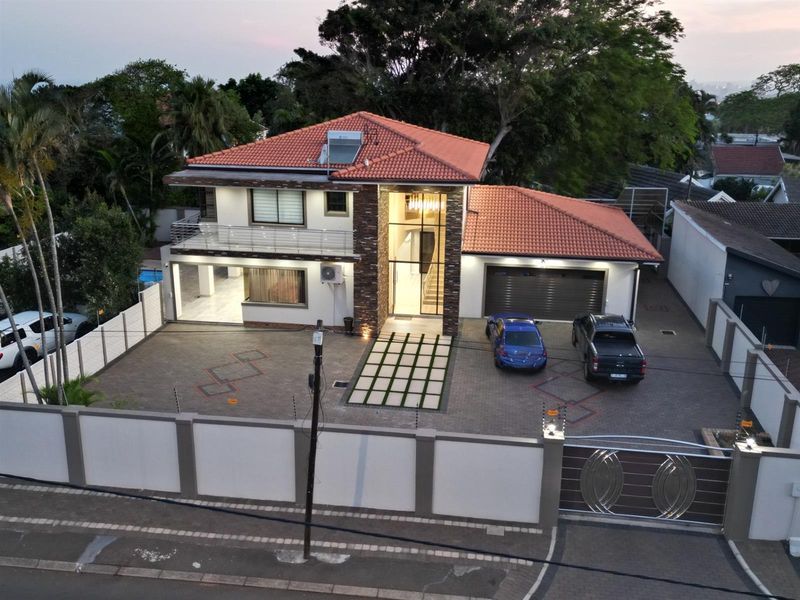 Aerial view of a modern double-story residence featuring a tiled roof, stone-clad facade, paved driveway, double garage, and secure perimeter walling.