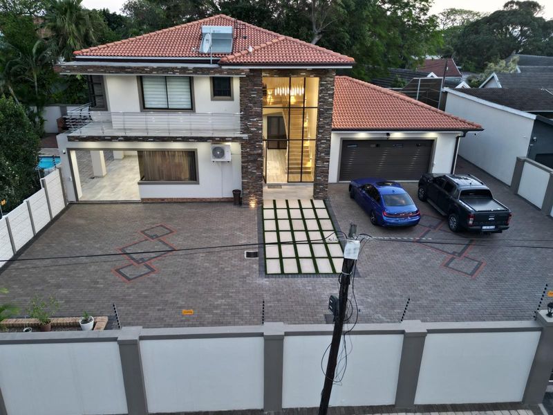 Modern double-story residence featuring a tiled roof, stone-clad entrance facade, paved driveway, double garage, and a balcony with stainless steel railings.