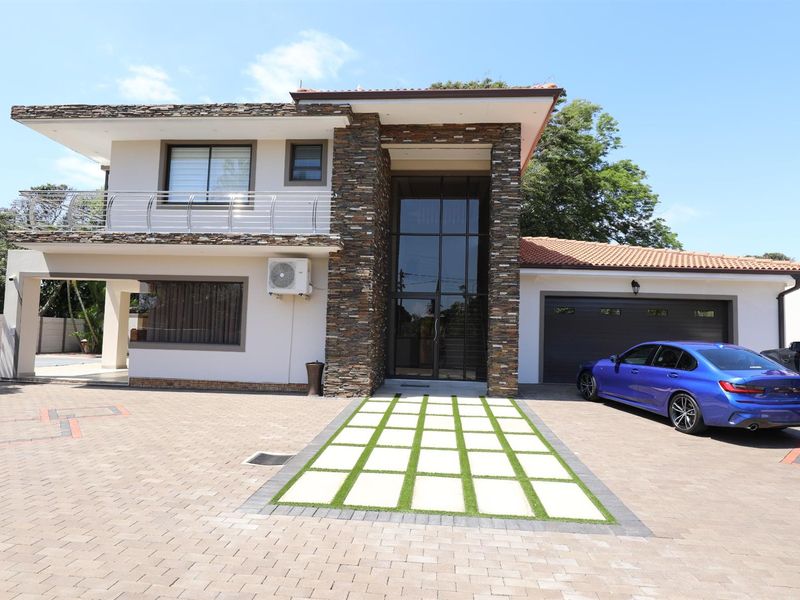 Modern double-story residence featuring stone cladding, large glass entrance, paved driveway, and an integrated double garage.