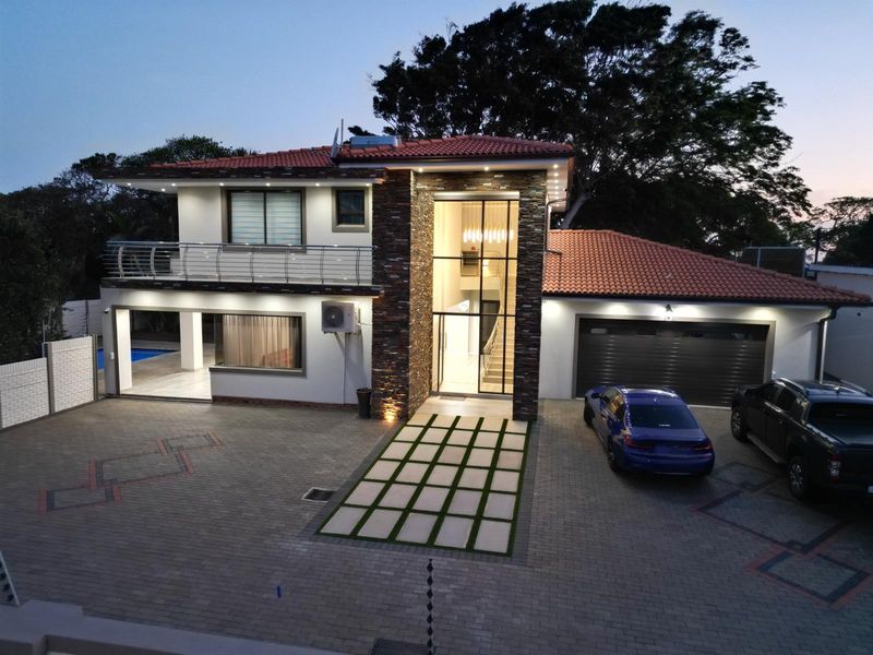 Modern double-story residence featuring a striking stone-clad entrance, tiled roof, paved driveway, integrated garage, and a balcony with stainless steel railings.