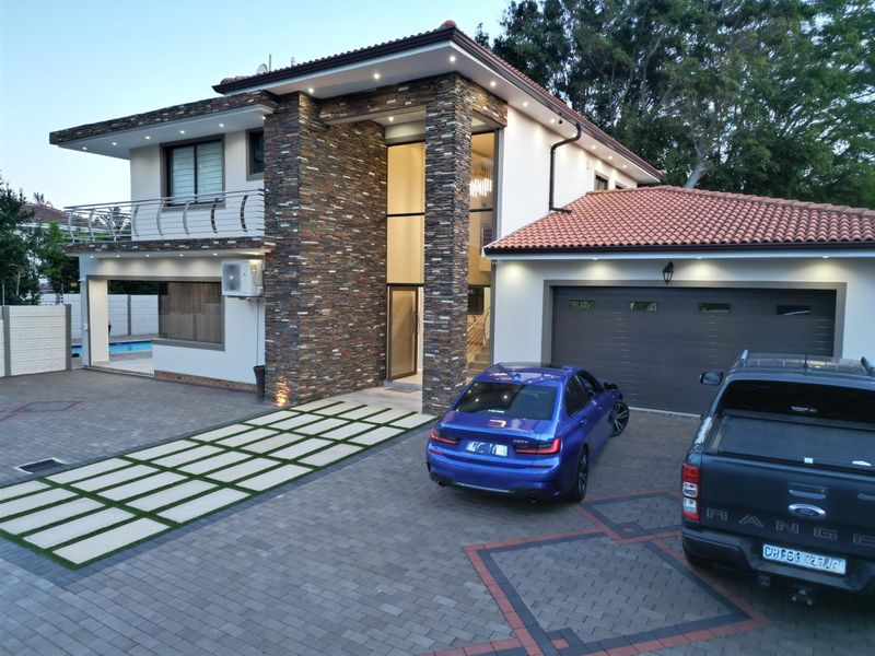 Modern double-story residence featuring stone-clad facade, tiled roof, paved driveway, integrated garage, and balcony overlooking the pool area.