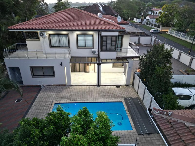 Aerial view of a two-story residential property featuring a tiled roof, upper-level balconies, a covered patio, and a swimming pool with paved surround.