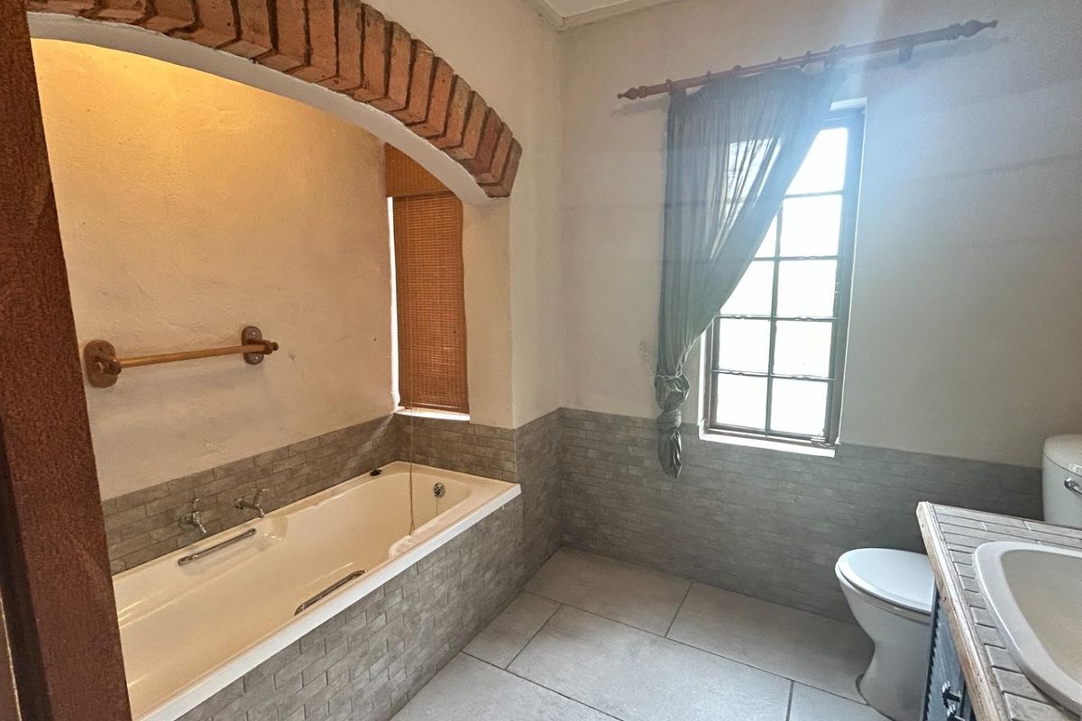 A bathroom featuring a built-in bathtub set under a brick archway, tiled flooring, and a standard toilet and vanity basin.