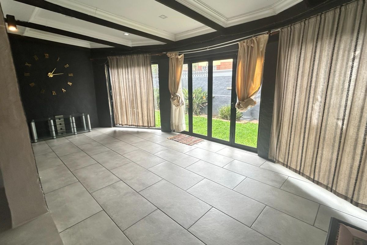 Spacious living area featuring large glass sliding doors, tiled flooring, and exposed ceiling beams, offering direct access to the rear garden.