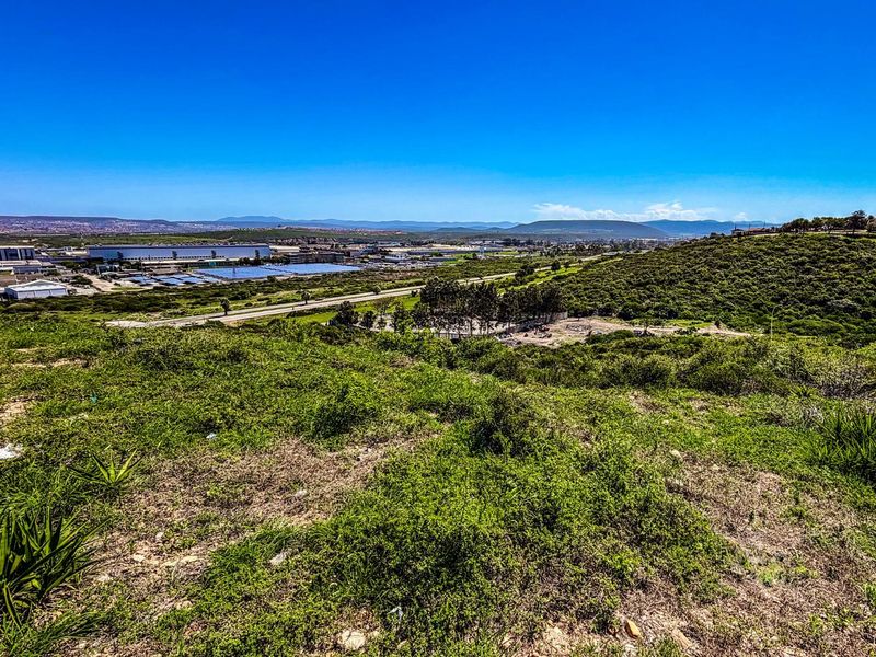 An elevated view overlooking a vacant residential plot with natural vegetation, featuring expansive landscape vistas and surrounding industrial and residential infrastructure.