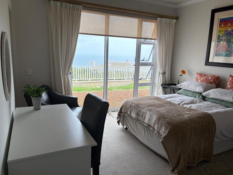 A bright bedroom featuring large sliding glass doors that open to a patio with scenic coastal views.