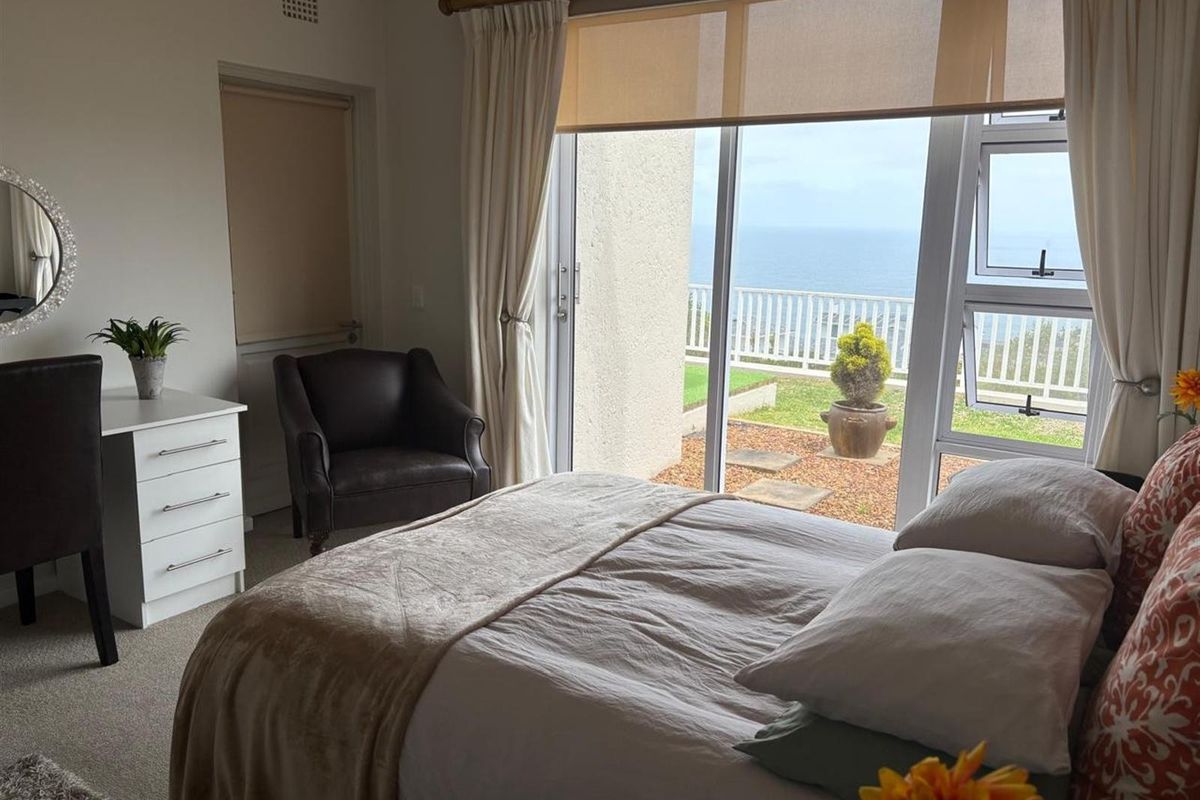 A bright bedroom featuring large sliding glass doors that open onto a private patio with scenic ocean views.