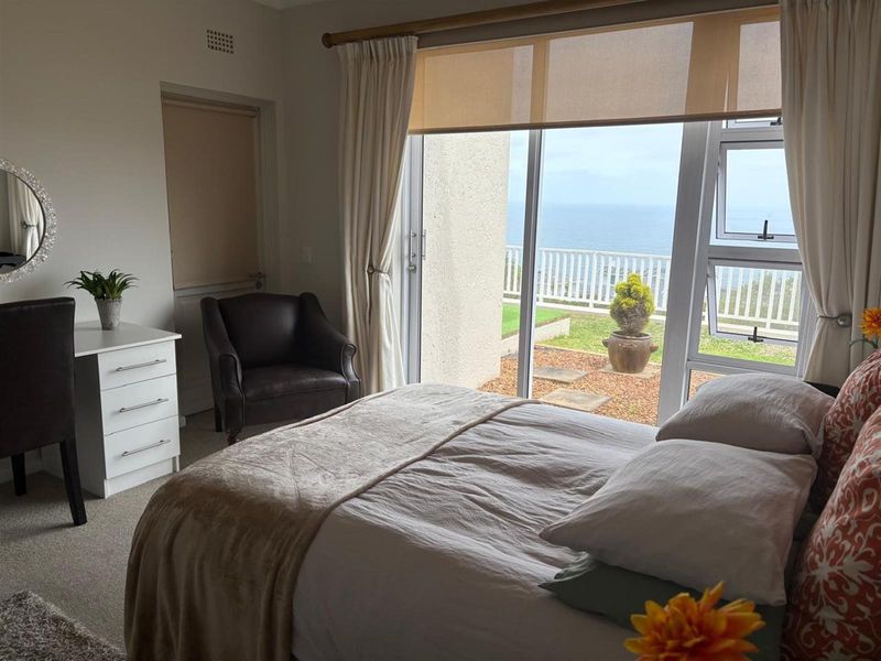 A bright bedroom featuring large sliding glass doors that open onto a private patio with scenic ocean views.