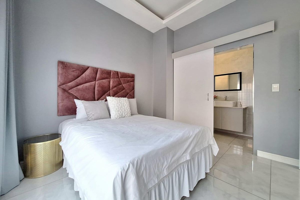 A modern bedroom featuring a tray ceiling, tiled flooring, and an en-suite bathroom accessed via a sliding door.