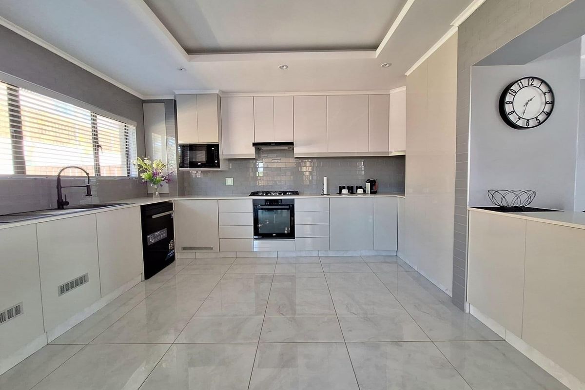 Modern kitchen featuring sleek white cabinetry, integrated oven and hob, subway tile backsplash, and large format floor tiles with recessed ceiling lighting.