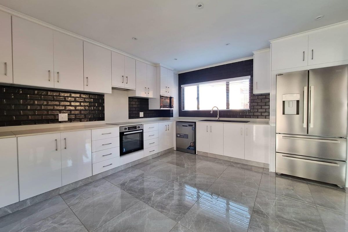 Modern kitchen featuring white cabinetry, dark subway tile backsplash, integrated oven, stainless steel dishwasher, and polished grey floor tiles.