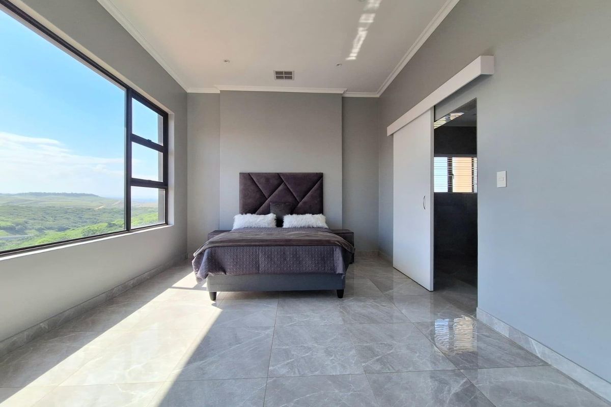 Spacious bedroom featuring large windows with scenic views, polished tile flooring, recessed lighting, and a sliding door leading to an en-suite bathroom.
