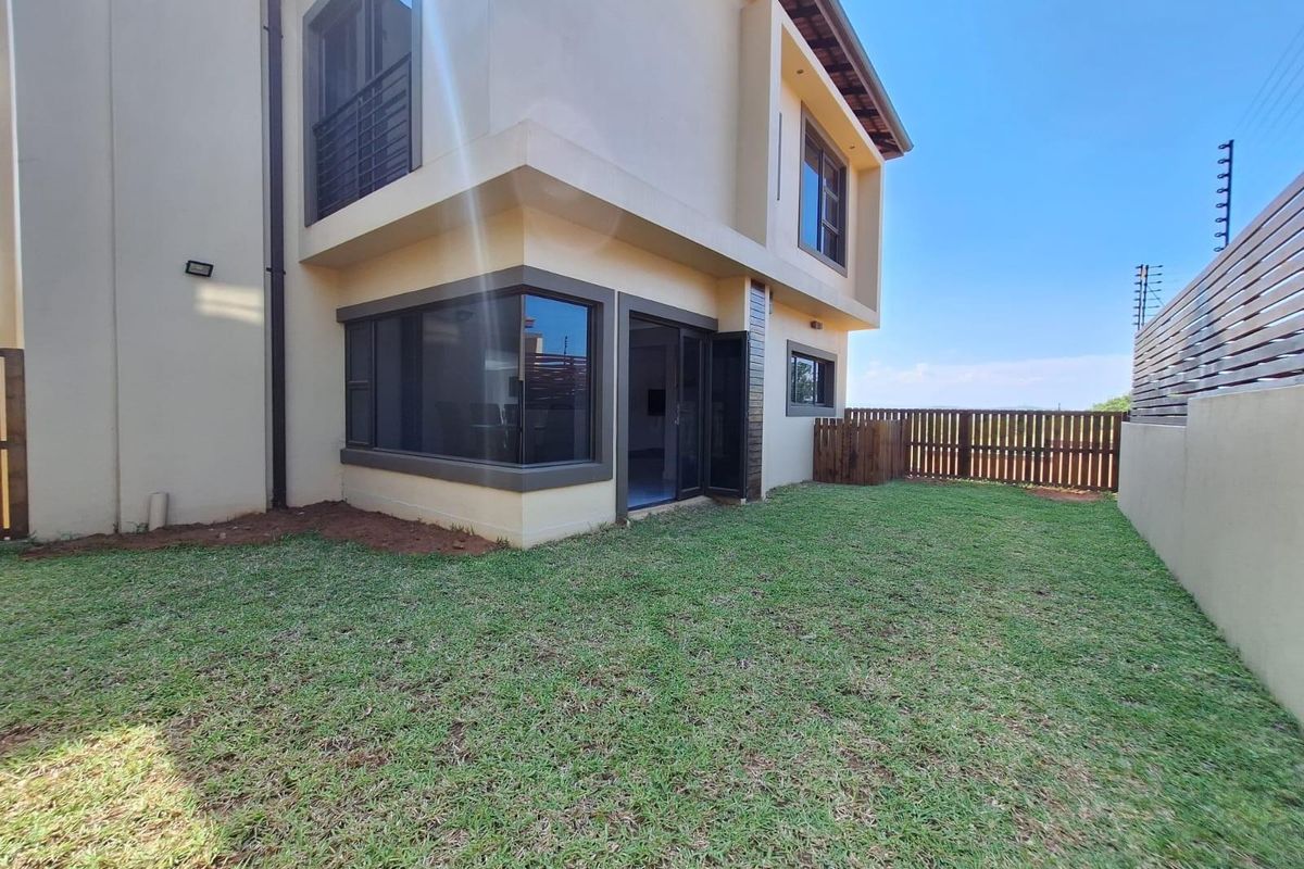 Rear view of a modern two-story house featuring a landscaped lawn, perimeter fencing, and large glass windows.