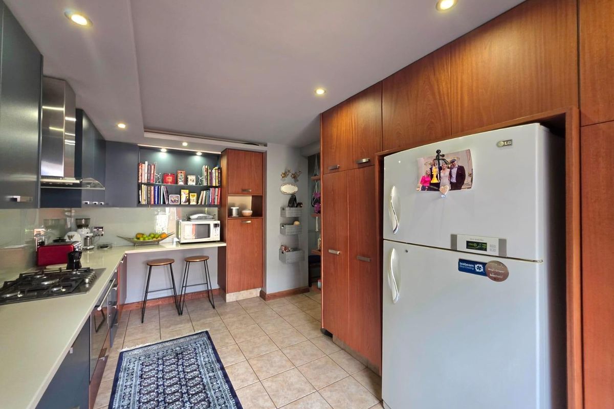 Modern kitchen featuring dark cabinetry, integrated wood-finish storage, stone countertops, a built-in gas hob, and a stainless steel extractor fan.