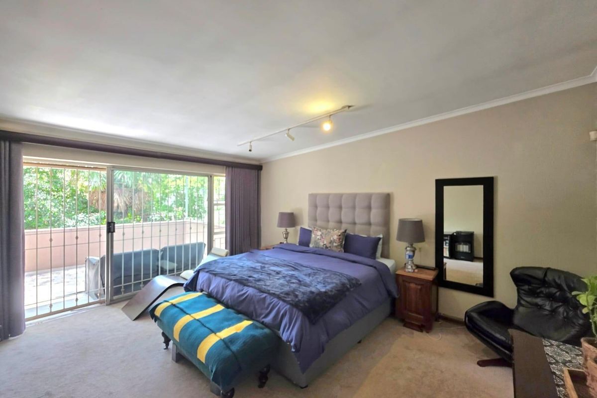 Spacious bedroom featuring large sliding glass doors with security gates, providing direct access to a private balcony and ample natural light.