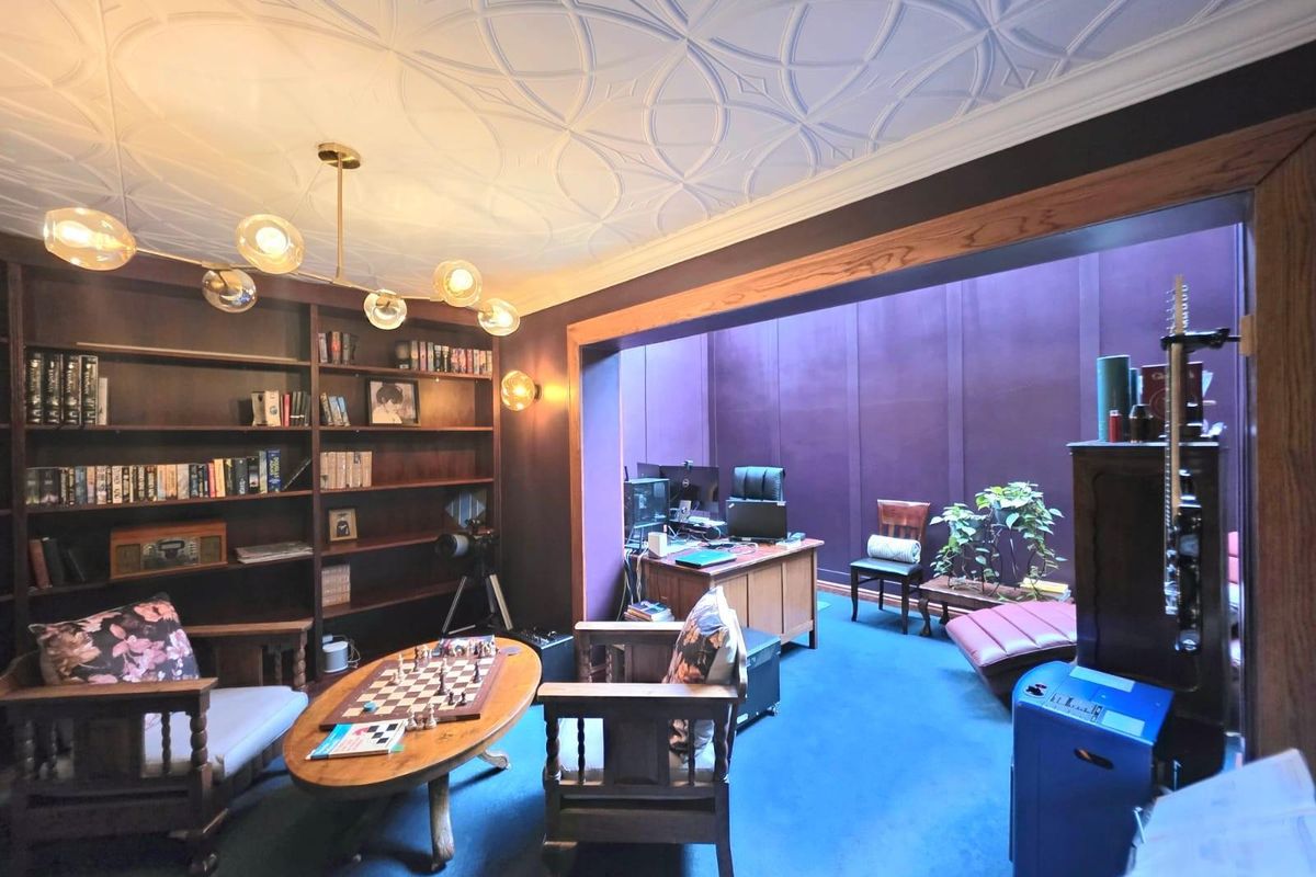 A spacious living area featuring built-in wooden shelving, a decorative patterned ceiling, and a large opening leading to an adjacent study or workspace.