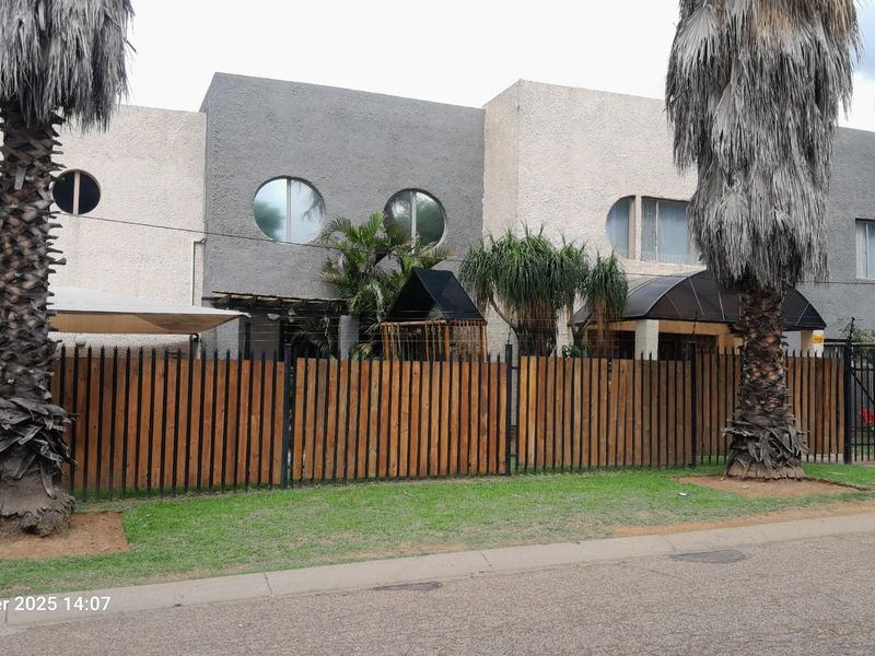 Street-facing view of a multi-level residential property featuring a wooden perimeter fence, circular windows, and a textured exterior facade.