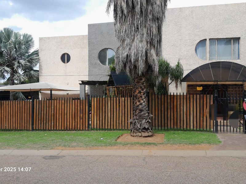 Front elevation of a multi-level residential property featuring unique circular windows, a wooden perimeter fence, and an arched entrance canopy.