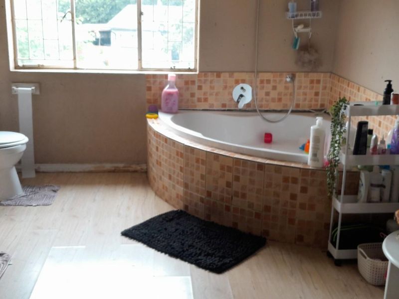 A dated bathroom featuring a corner bathtub with mosaic tiling, a standard toilet, and laminate flooring, offering potential for a modern renovation.