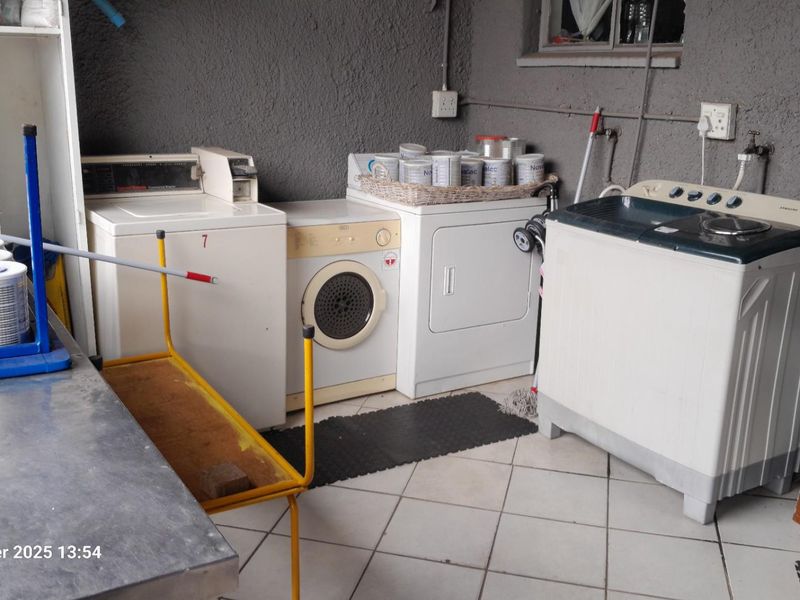 A functional laundry area featuring tiled flooring, a concrete utility sink, and multiple appliance connections against a textured wall finish.