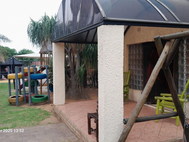 A covered patio area featuring tiled flooring and a curved polycarbonate roof structure, overlooking a garden space with play equipment.