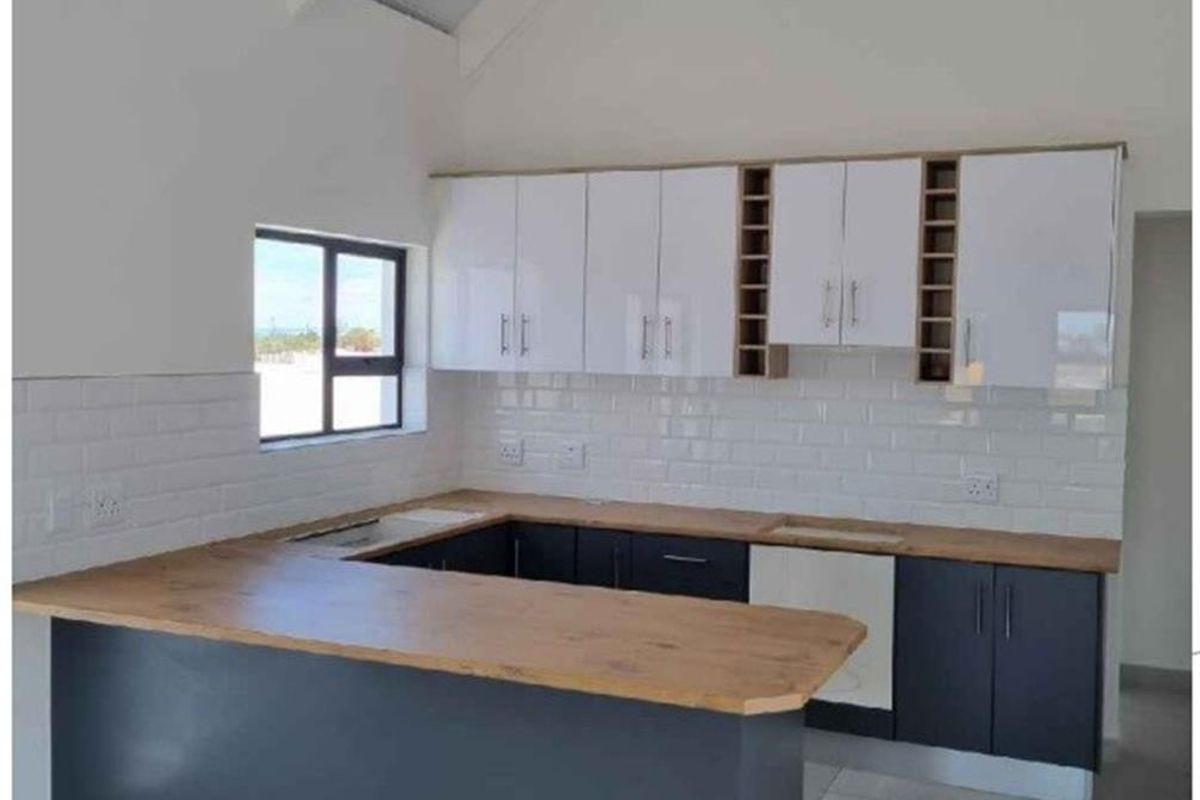 Modern kitchen featuring a U-shaped layout with dark cabinetry, light wood countertops, white subway tile backsplash, and high vaulted ceilings.