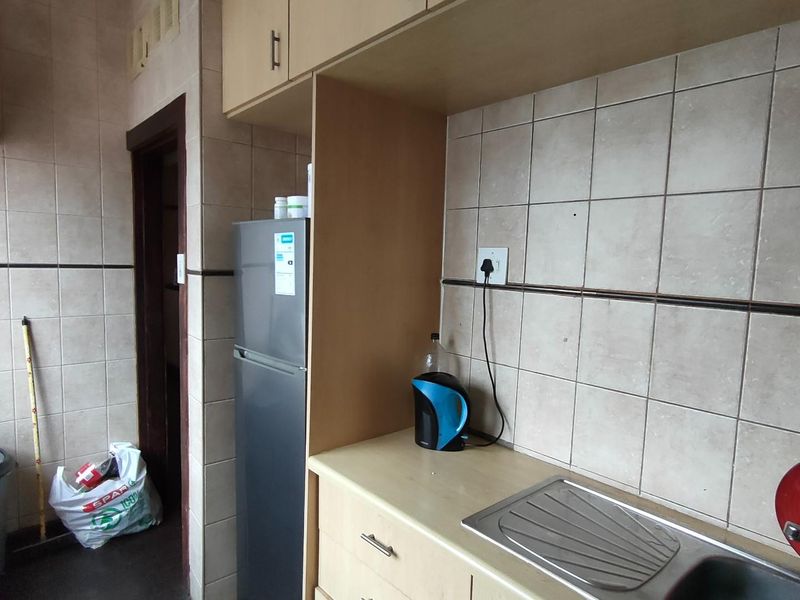 A functional kitchen area featuring tiled walls, built-in cabinetry, and a stainless steel sink, offering a practical layout for daily meal preparation.