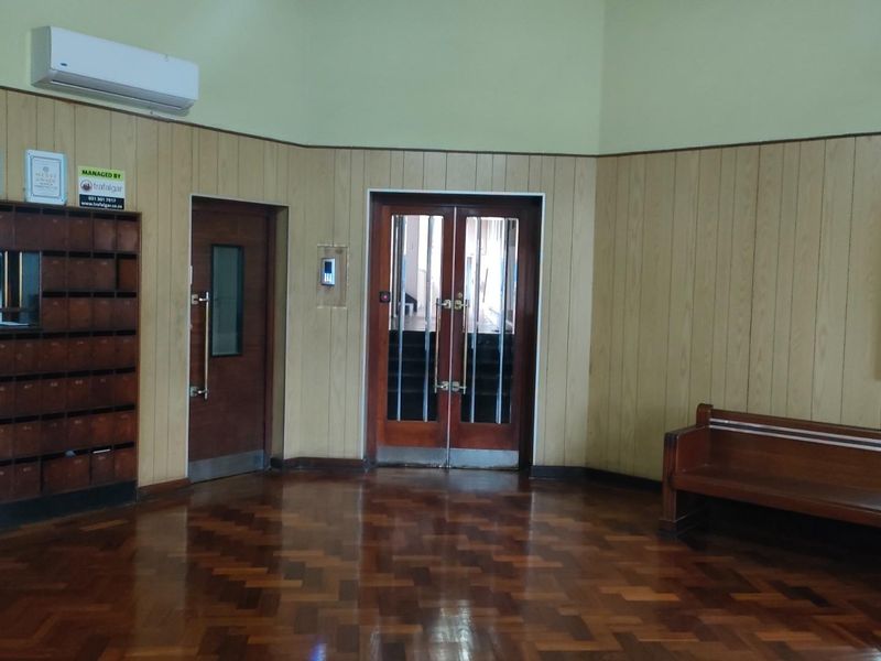 A communal apartment building lobby featuring parquet flooring, wood wall paneling, built-in mailboxes, and secure double-door access.