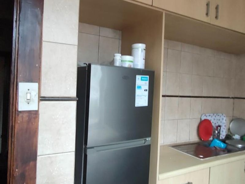 A functional kitchen area featuring light wood-toned cabinetry, tiled splashbacks, and a dedicated space for a refrigerator.