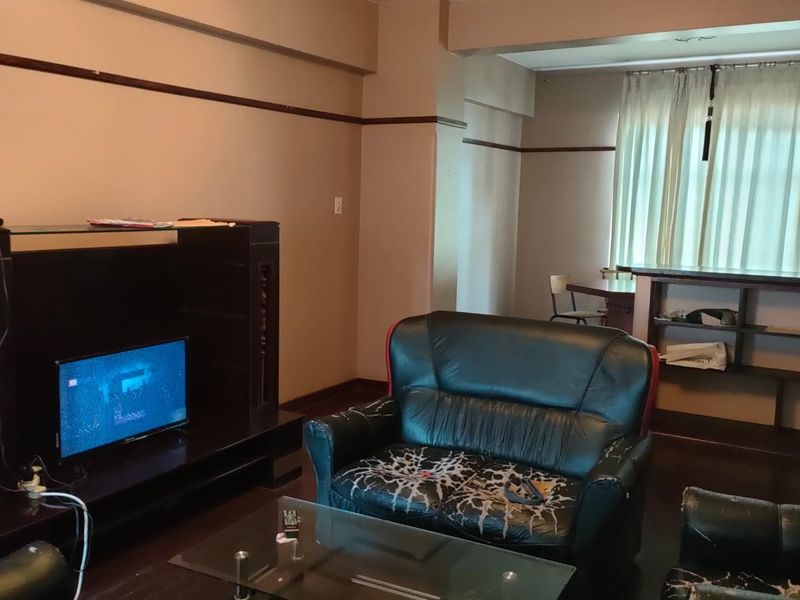A spacious living area featuring dark wood-style flooring, neutral wall tones, and a built-in shelving unit, offering a functional layout for relaxation.
