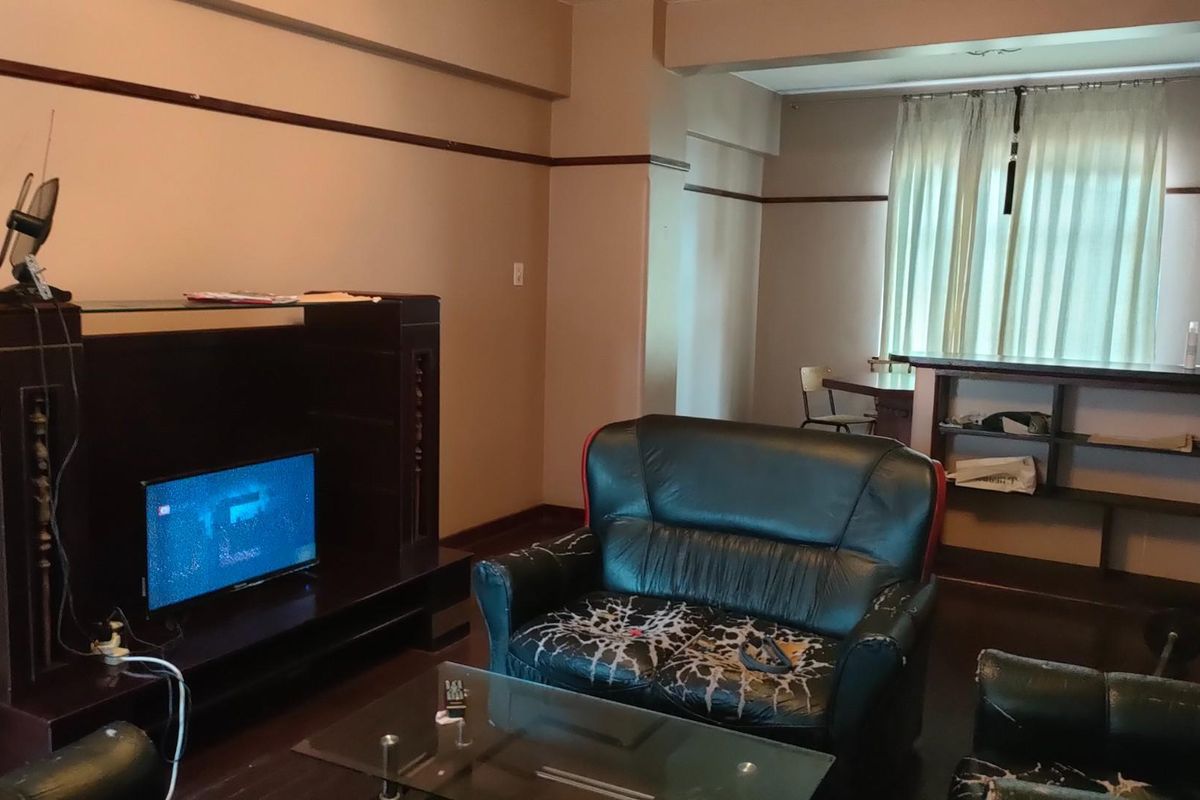 A spacious living area featuring dark wood-style flooring, neutral wall tones, and a built-in shelving unit, offering a functional layout for relaxation.