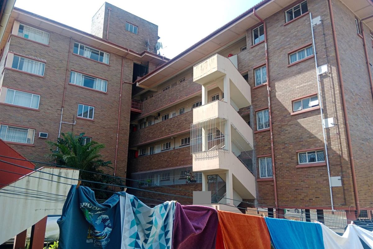 Exterior view of a multi-story brick apartment building featuring a central concrete stairwell and residential window units.
