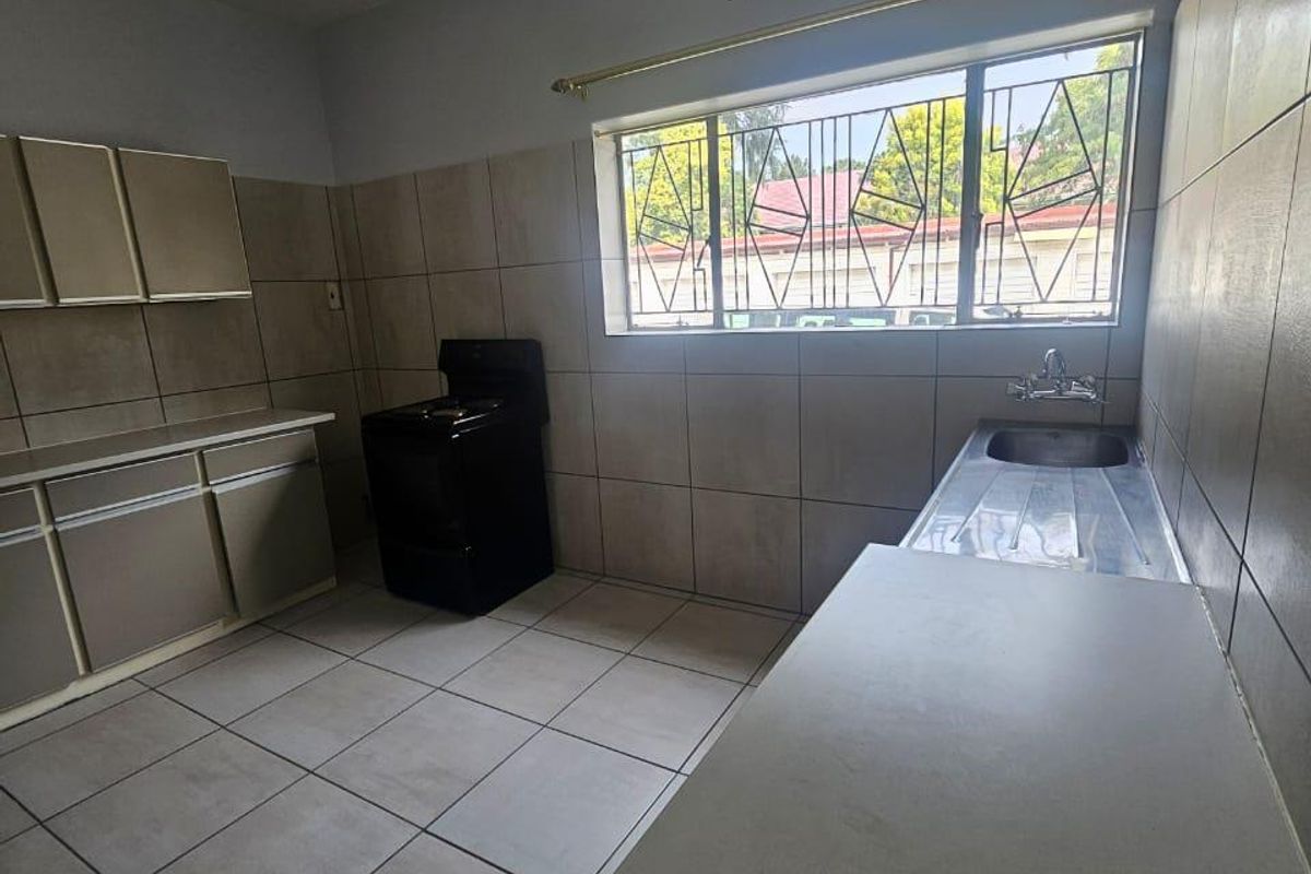 A functional kitchen featuring tiled walls and flooring, built-in cabinetry, a stainless steel sink, and a window with security bars.