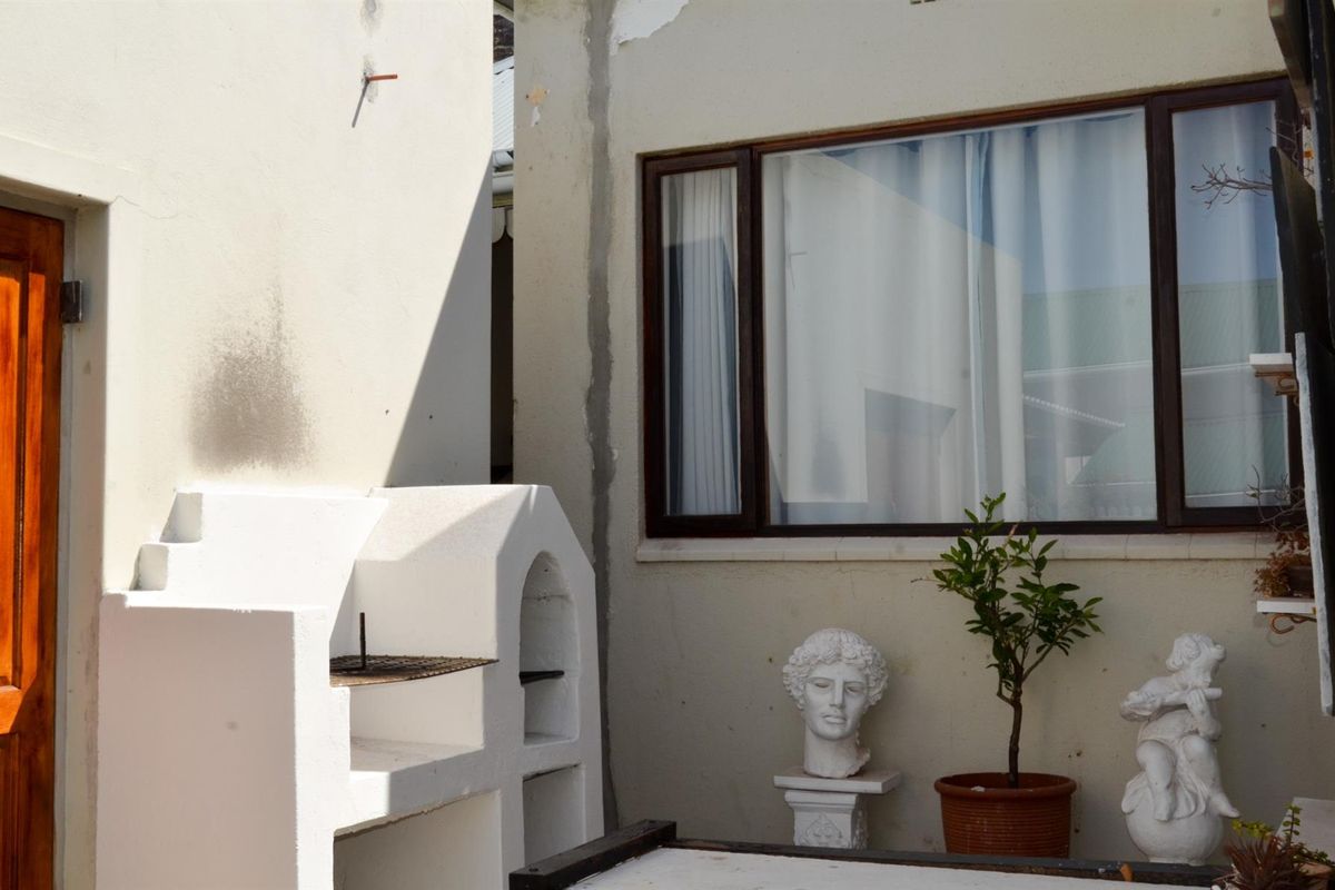 Rear courtyard area featuring a built-in braai, timber-framed window, and timber door, requiring some exterior maintenance and plaster repair.