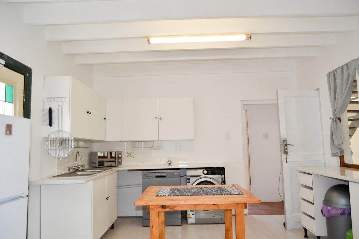 Functional kitchen featuring white built-in cabinetry, stainless steel sink, tiled splashback, and exposed ceiling beams, offering a practical layout for daily use.