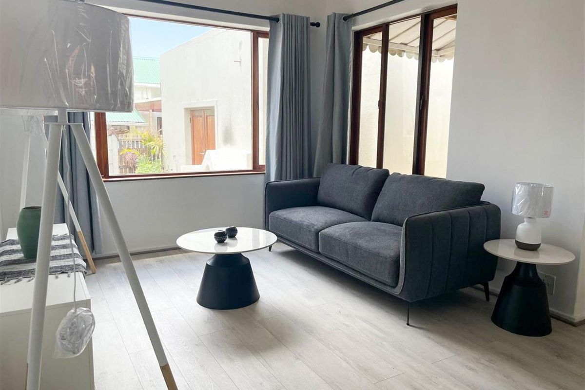 A bright and modern living room featuring light-toned laminate flooring and large windows with timber frames, offering a clean and neutral aesthetic.