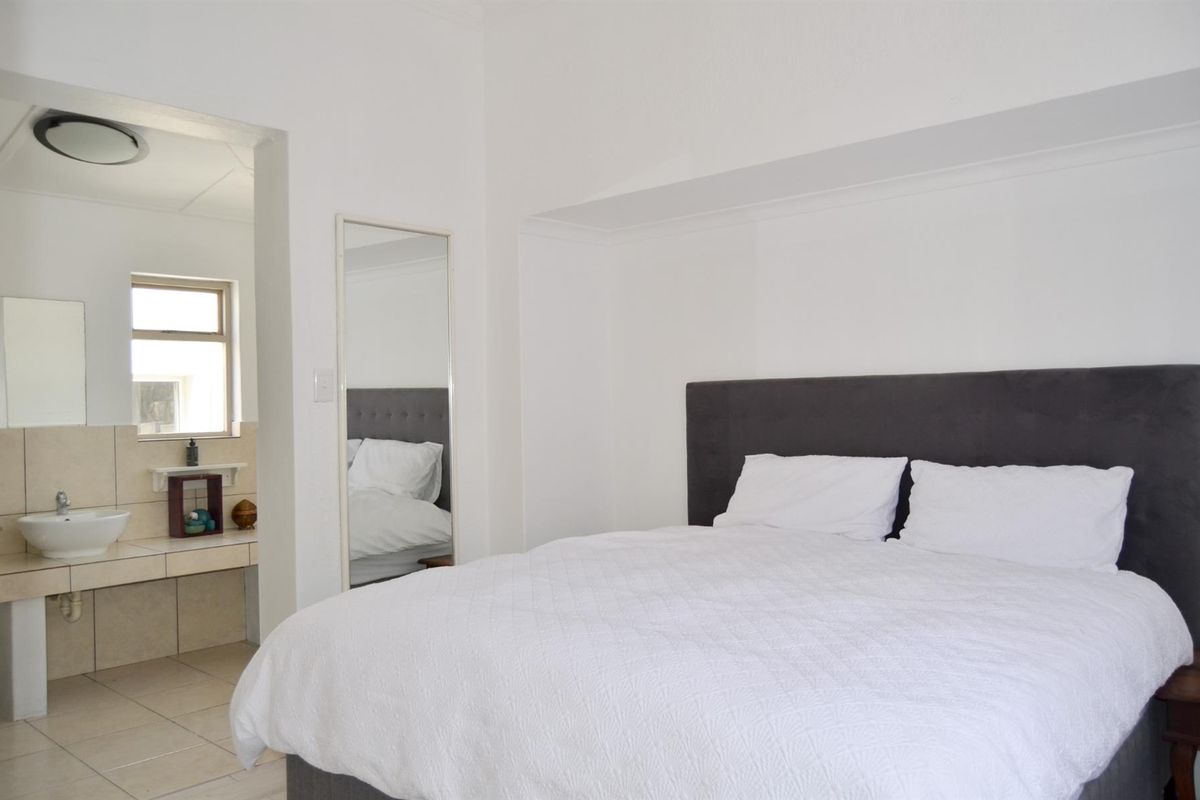 A bright bedroom featuring an open-plan en-suite bathroom with tiled finishes and a neutral interior design.