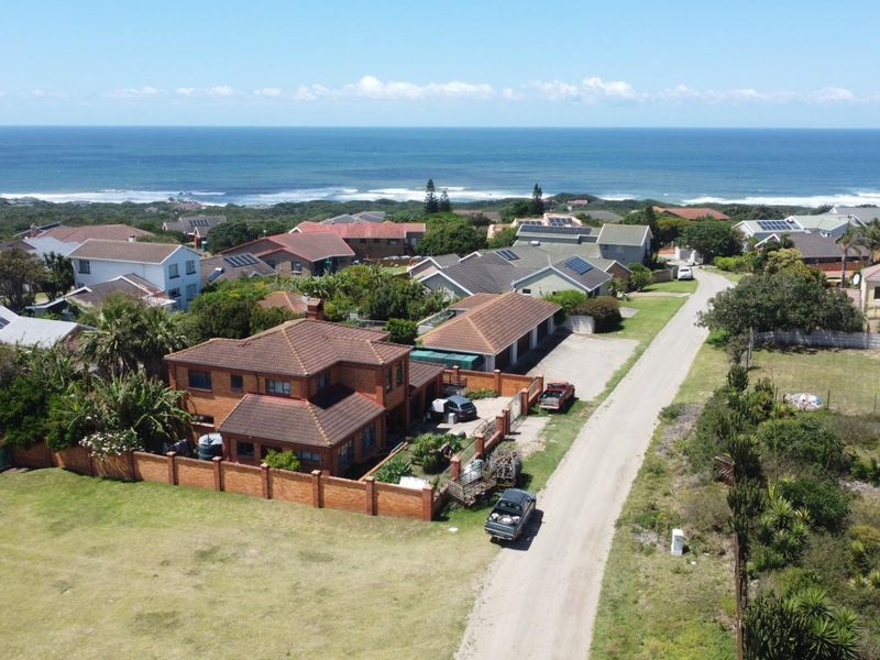 Aerial view of a residential property featuring a brick house, perimeter wall, and surrounding coastal landscape with ocean views.