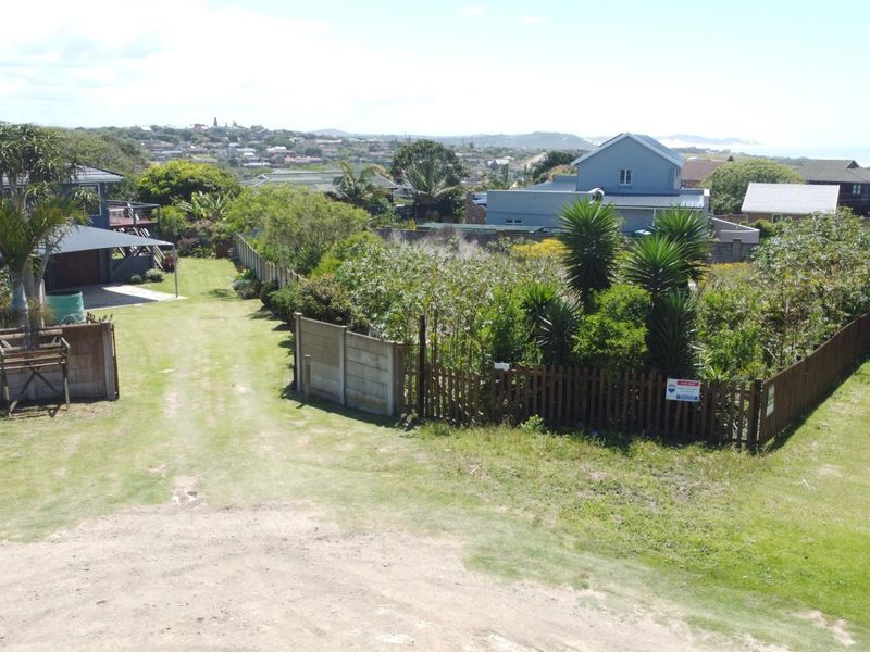 An elevated view of a residential vacant land plot featuring established perimeter fencing, mature garden vegetation, and water storage tanks.