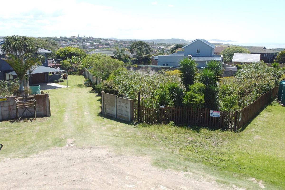 An elevated view of a residential vacant land plot featuring established perimeter fencing, mature garden vegetation, and water storage tanks.