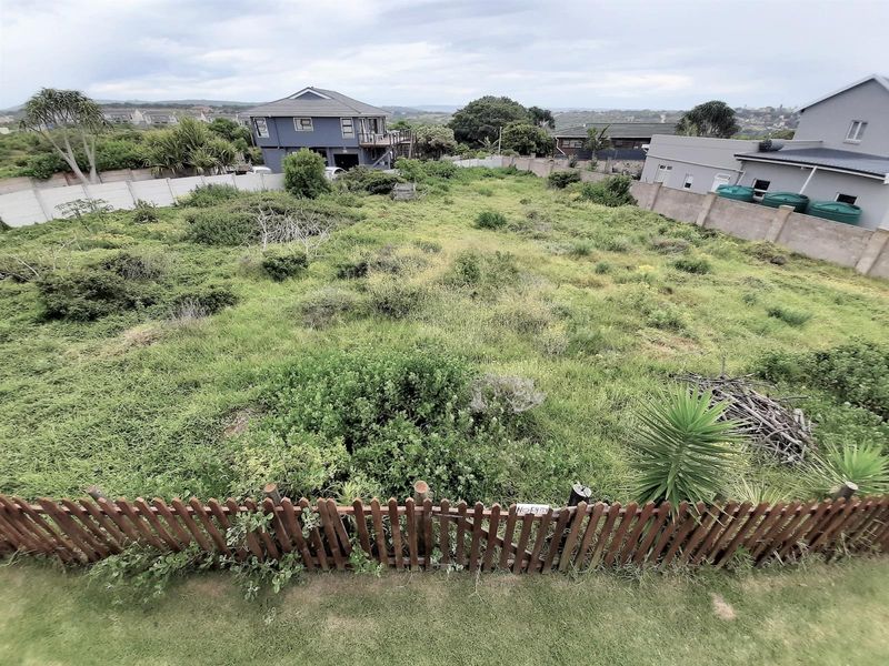 An elevated view of a vacant residential plot featuring overgrown vegetation, enclosed by perimeter walls and a wooden fence.