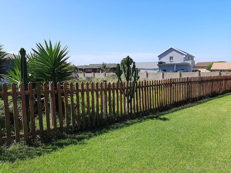 A view of a vacant residential plot featuring a wooden picket fence, established lawn, and surrounding boundary walls.