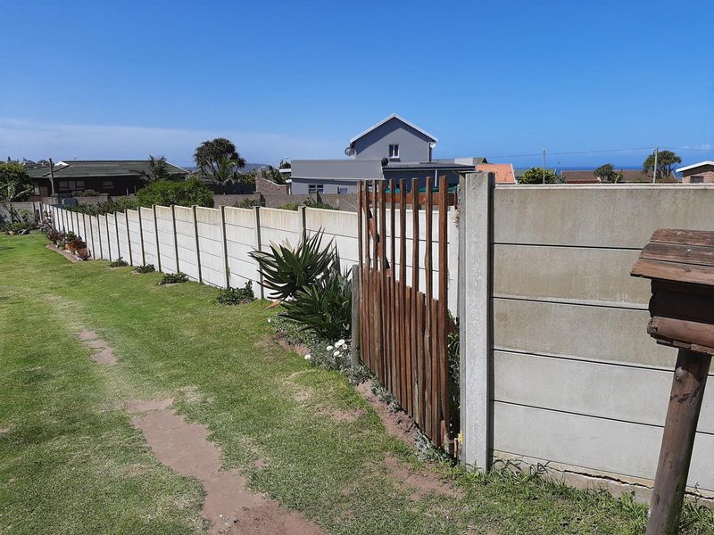 A view of a residential property boundary featuring a long concrete wall, a wooden pedestrian gate, and a well-maintained lawn area.