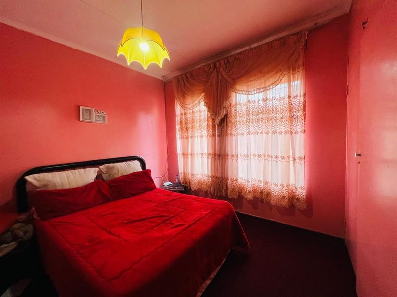 A bedroom featuring pink walls, a window with decorative curtains, and a central pendant light fixture.