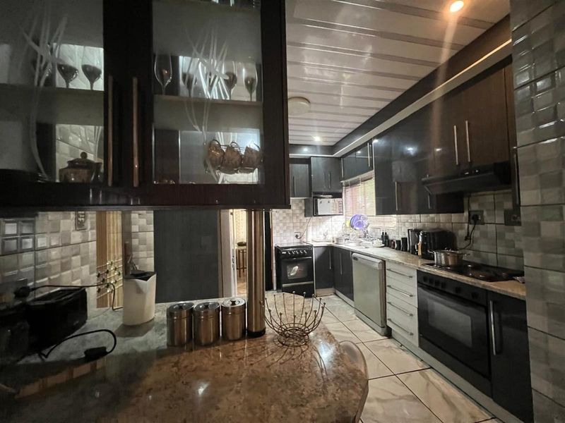 A functional kitchen featuring dark cabinetry, granite countertops, tiled backsplash, built-in oven, and hob, with a breakfast bar area.