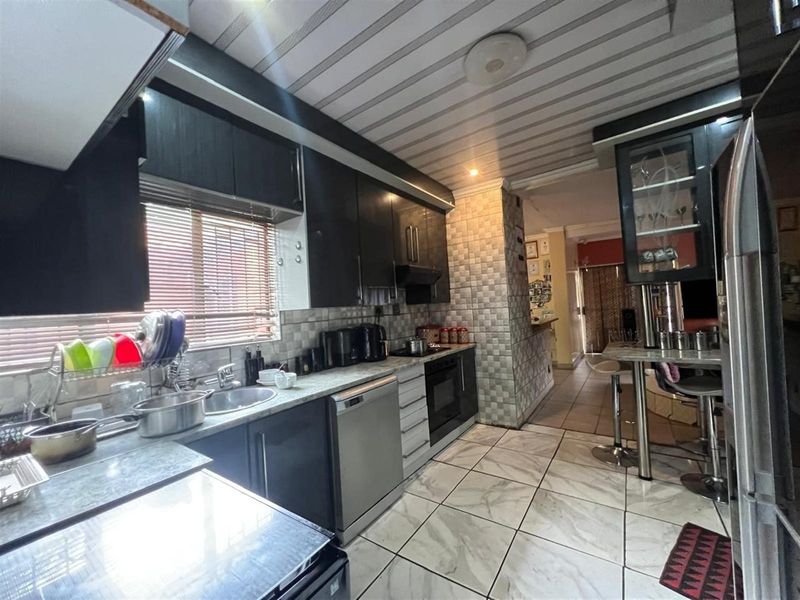 A functional kitchen featuring dark cabinetry, stone-look countertops, integrated oven, and tiled flooring, leading into an adjacent living area.