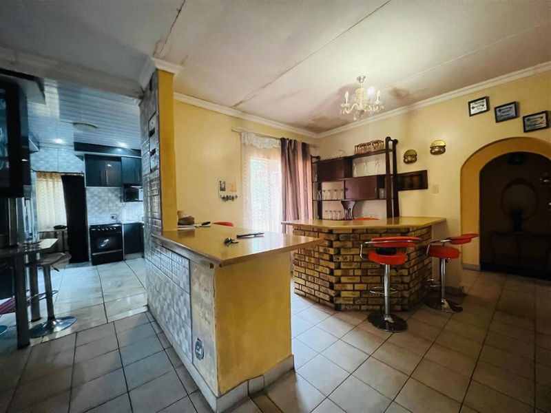 Open plan living area featuring a built-in brick bar counter and tiled flooring, with an adjacent kitchen visible in the background.