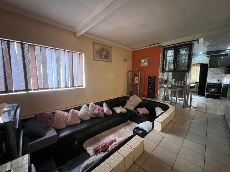 Open plan living area featuring a sunken lounge with tiled surround and an adjacent kitchen with built-in cabinetry and tiled flooring.