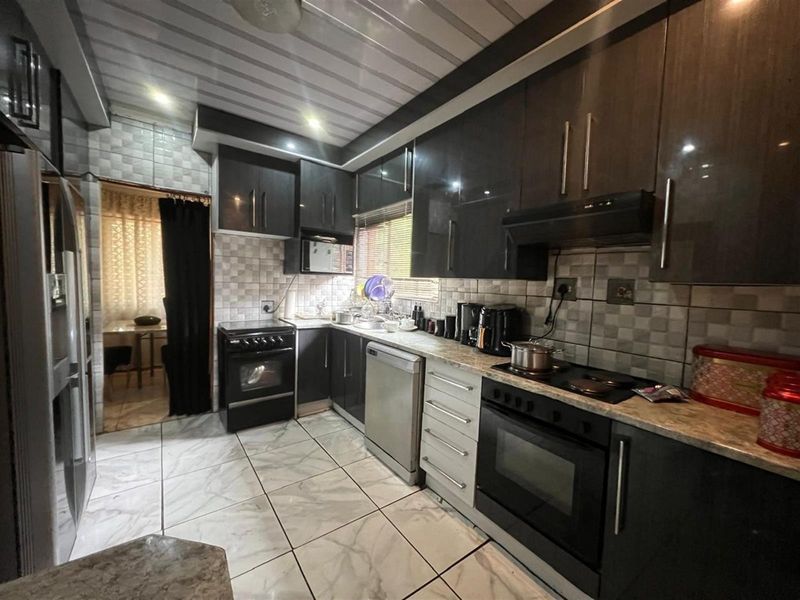 Modern kitchen featuring dark cabinetry, stone-look countertops, built-in oven, hob, and extractor fan with tiled flooring and backsplash.
